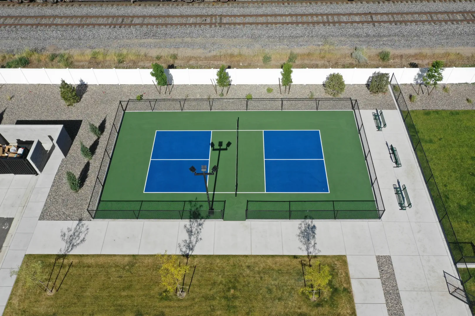Aerial view of a blue and green pickleball court with benches and a nearby train track.