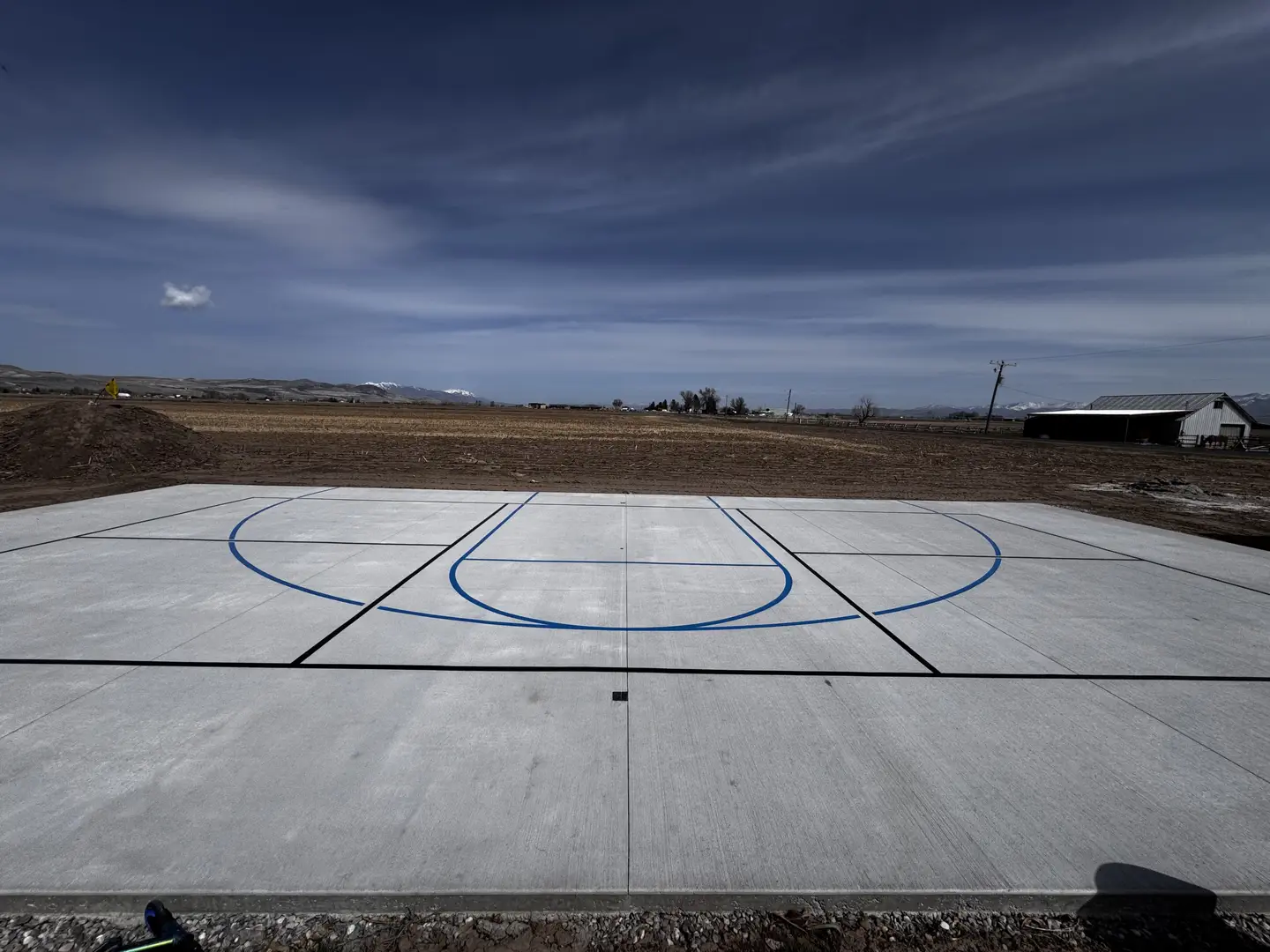 Newly constructed outdoor basketball court with blue lines in a rural setting.