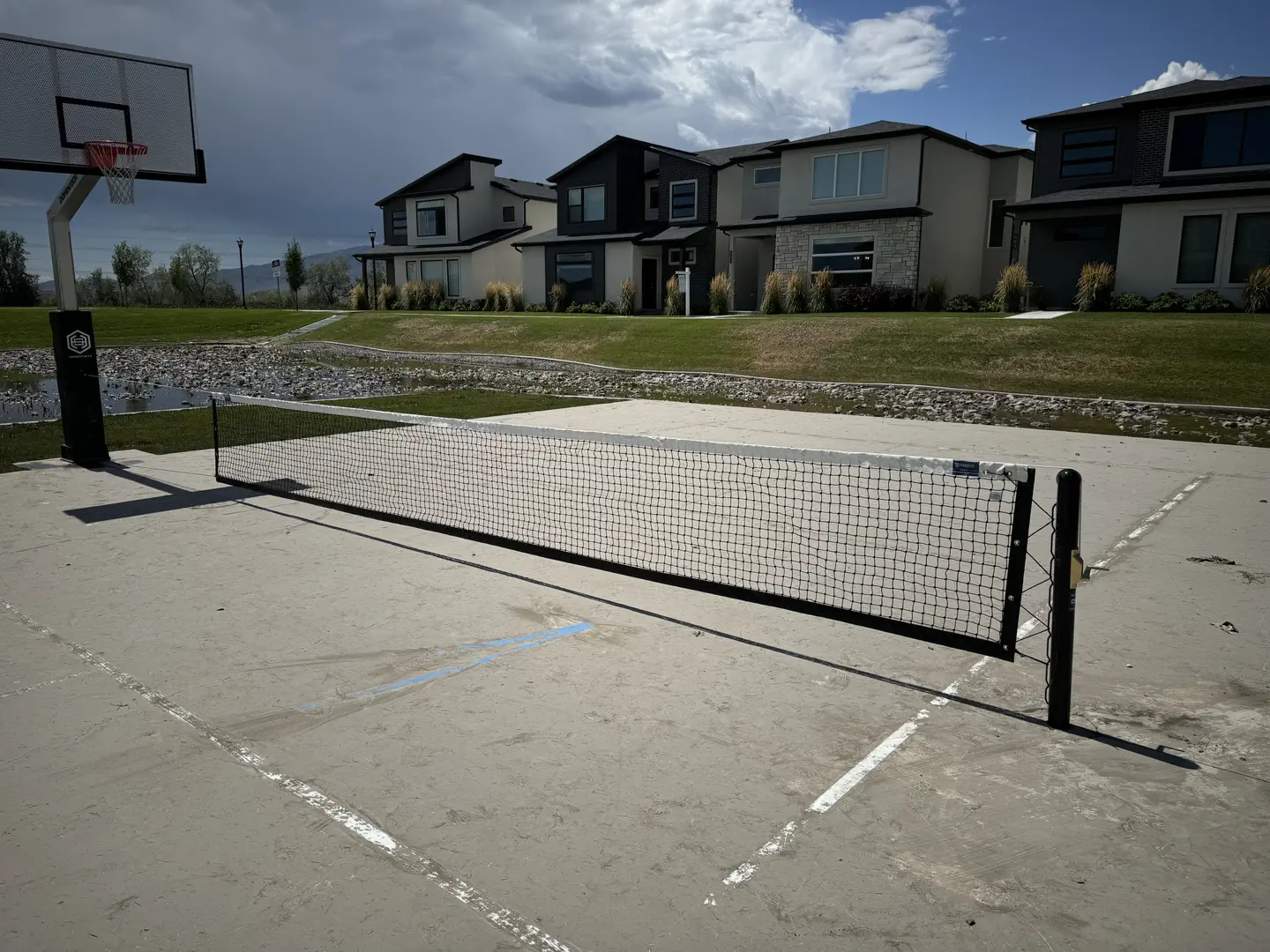 Outdoor pickleball court with basketball hoop and modern homes in background