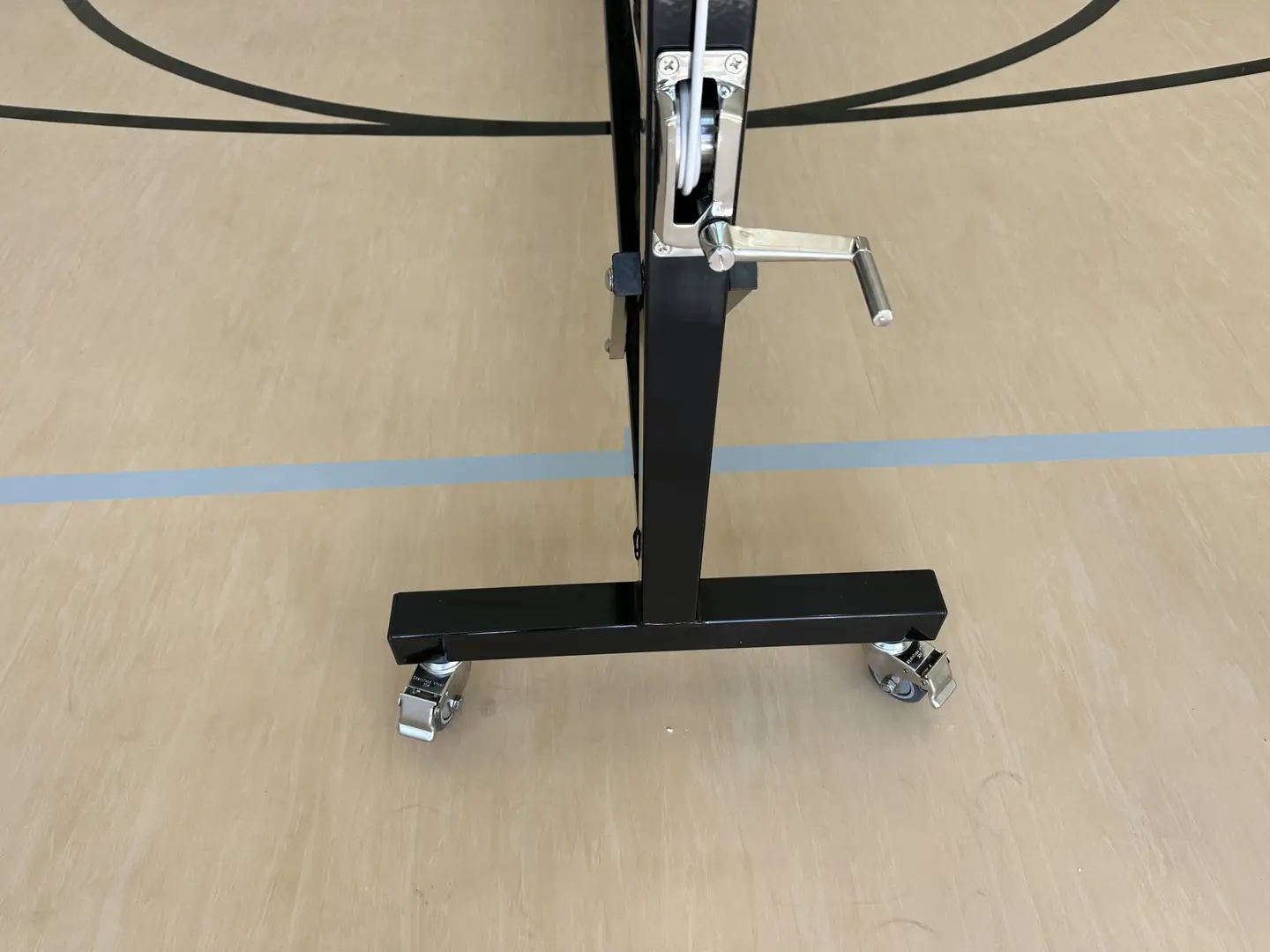 Close-up of a portable basketball hoop base with wheels on a gym floor.