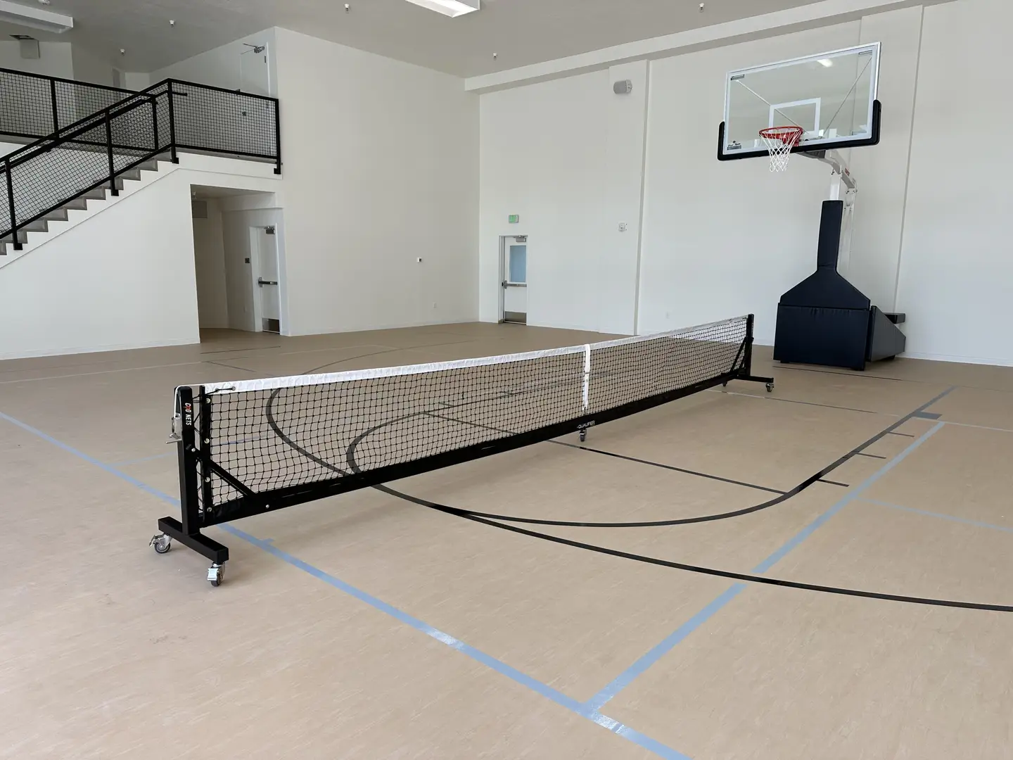 Indoor gymnasium with basketball hoop and portable net for sports like pickleball or volleyball.
