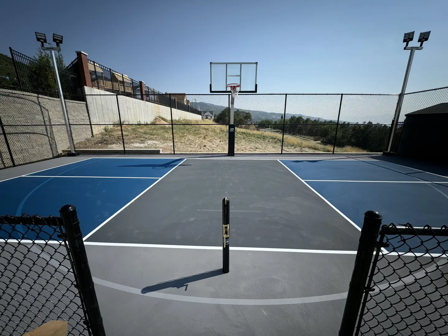 Multi-sport court with basketball hoop and pickleball lines, featuring blue and gray surfaces.