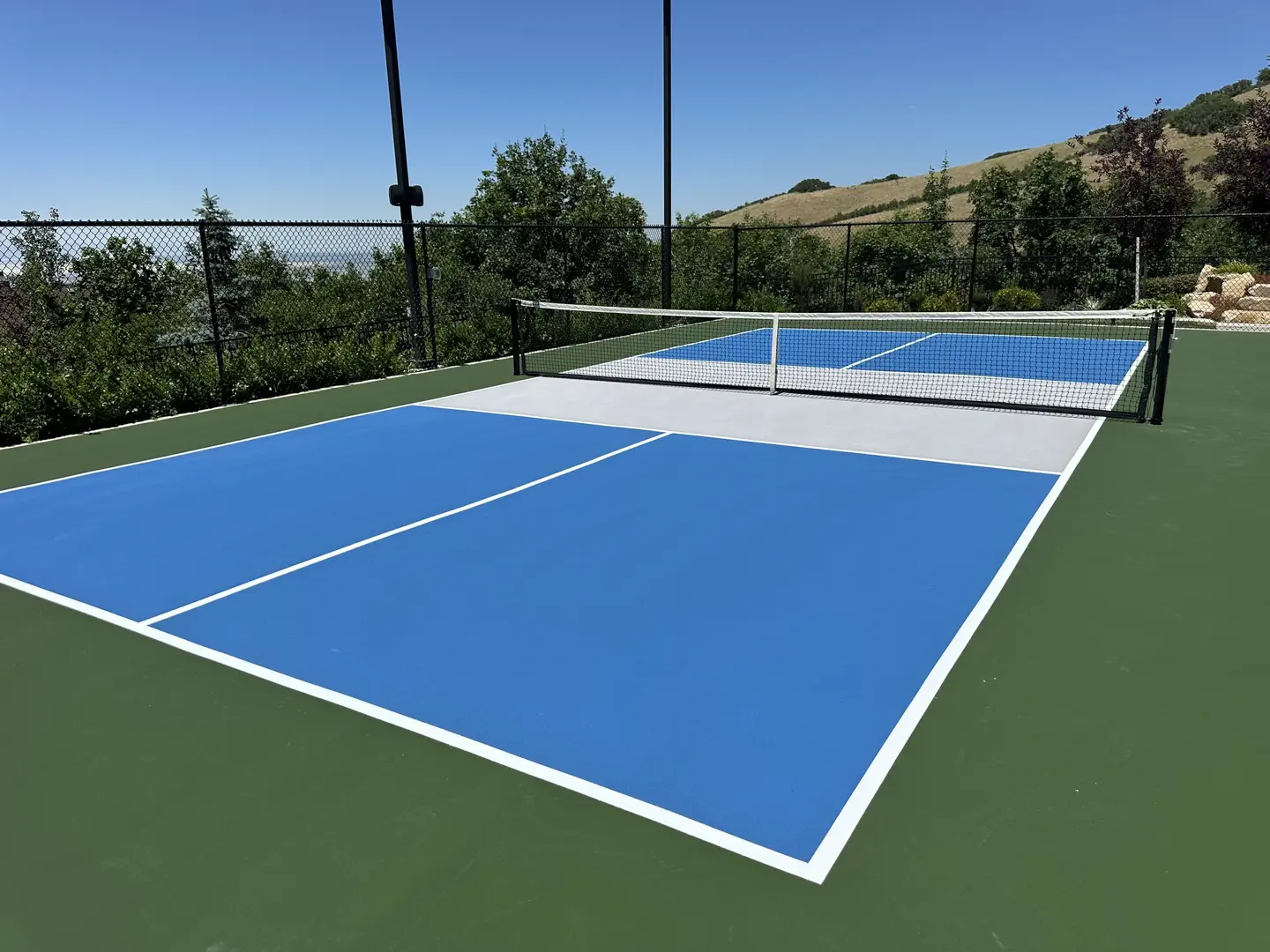 Bright blue pickleball court with green surround and mountain backdrop