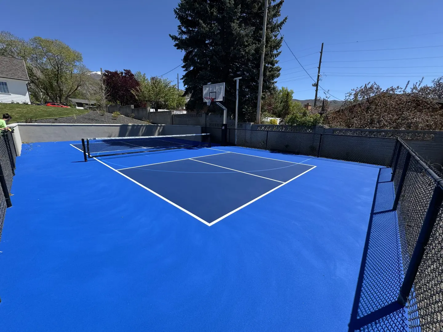 Vibrant blue pickleball court with a basketball hoop in the background.