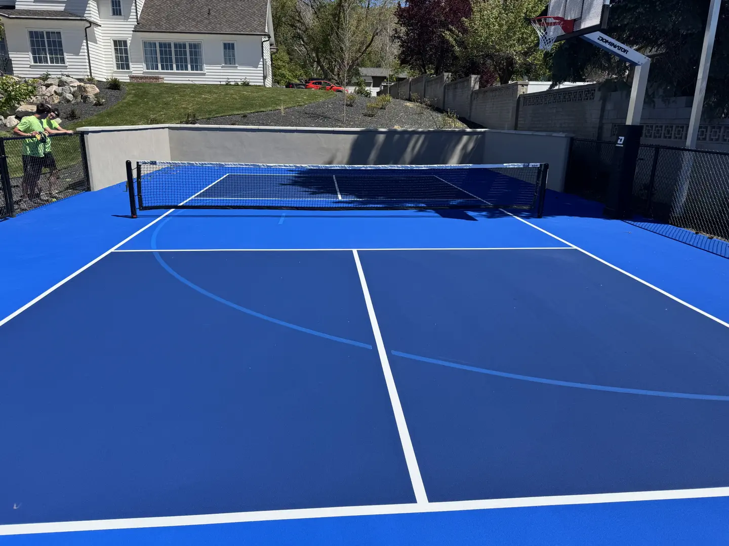 Vibrant blue pickleball court with a basketball hoop in the background.