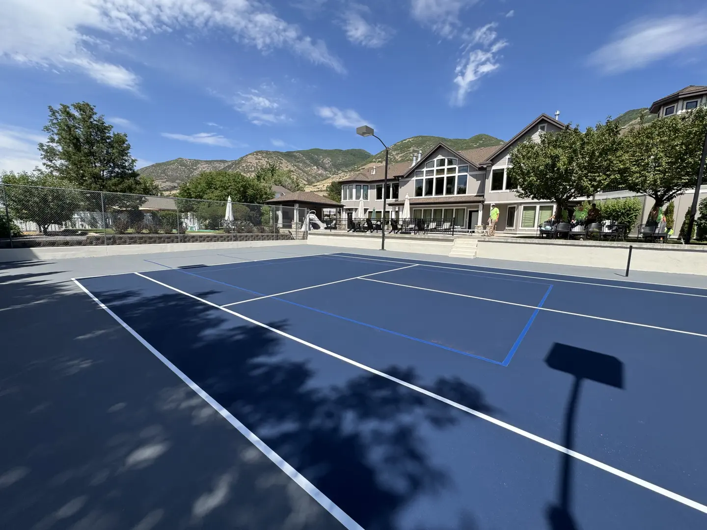 Newly resurfaced blue tennis court with white lines and a large house in the background.