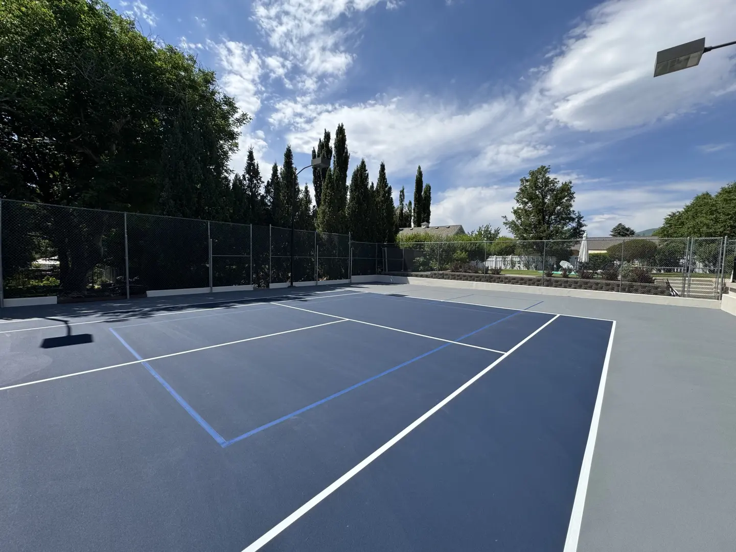 Newly resurfaced blue tennis court with white lines and surrounding fence.