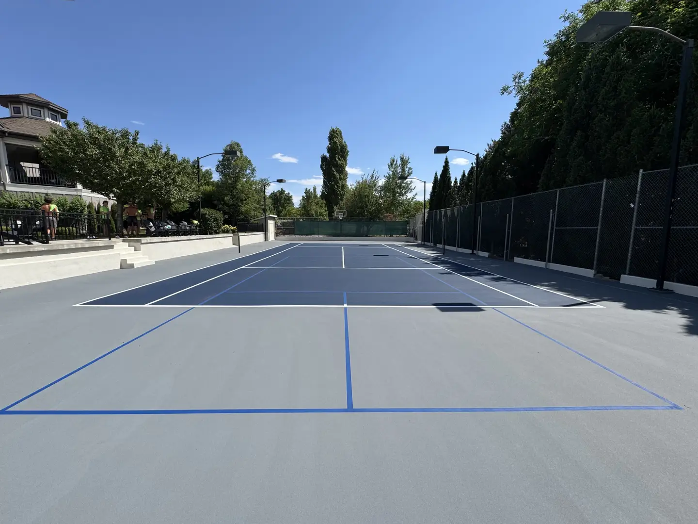 Newly resurfaced tennis court with blue and grey surfacing and white lines.