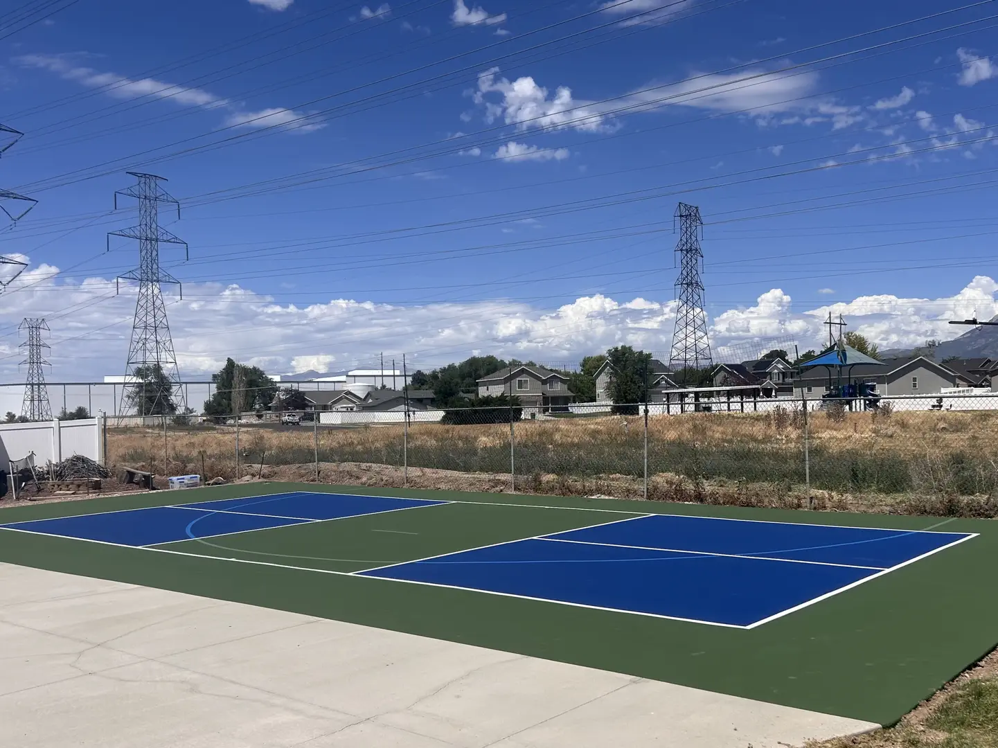 New blue and green pickleball court with power lines in the background.
