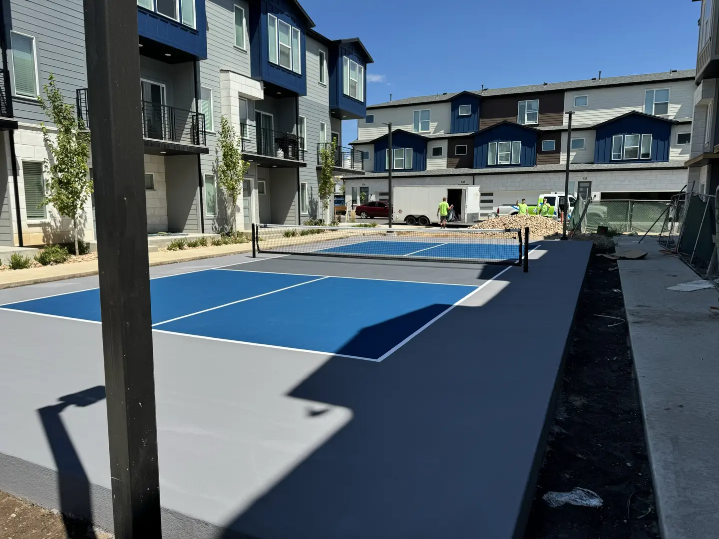 Newly painted pickleball court with blue and gray surfaces next to apartment buildings.