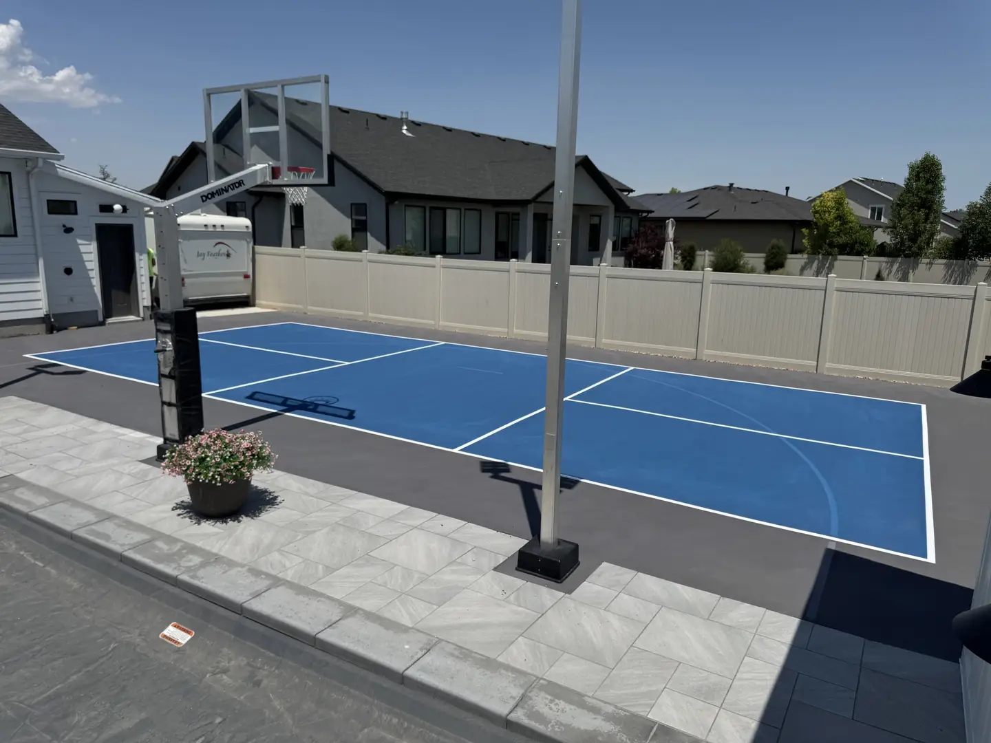 Blue backyard basketball court with white lines and a basketball hoop.