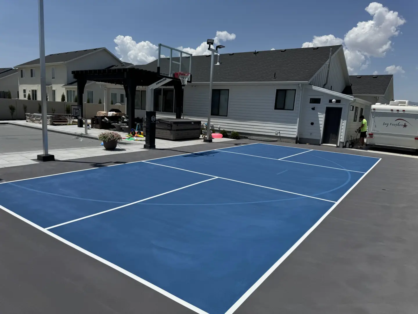 Bright blue basketball court with white lines in a suburban backyard.