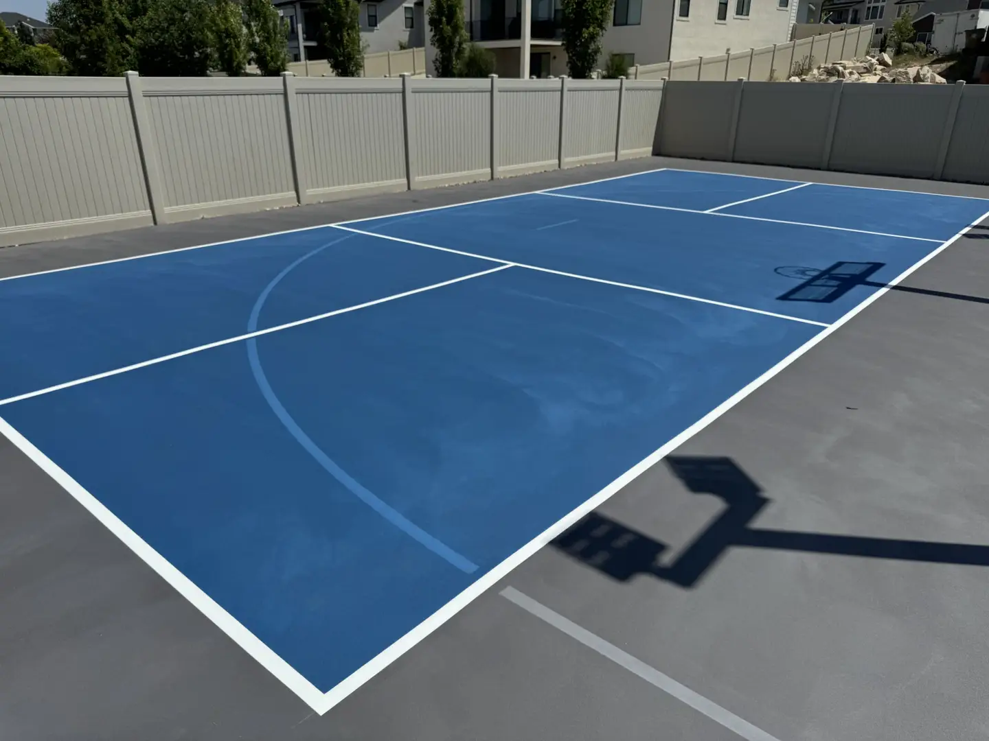 Blue basketball court with white lines and a hoop in a backyard.