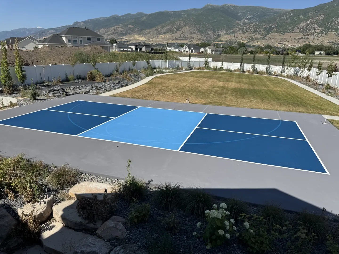Blue and light blue multi-sport court with white lines, backyard setting.