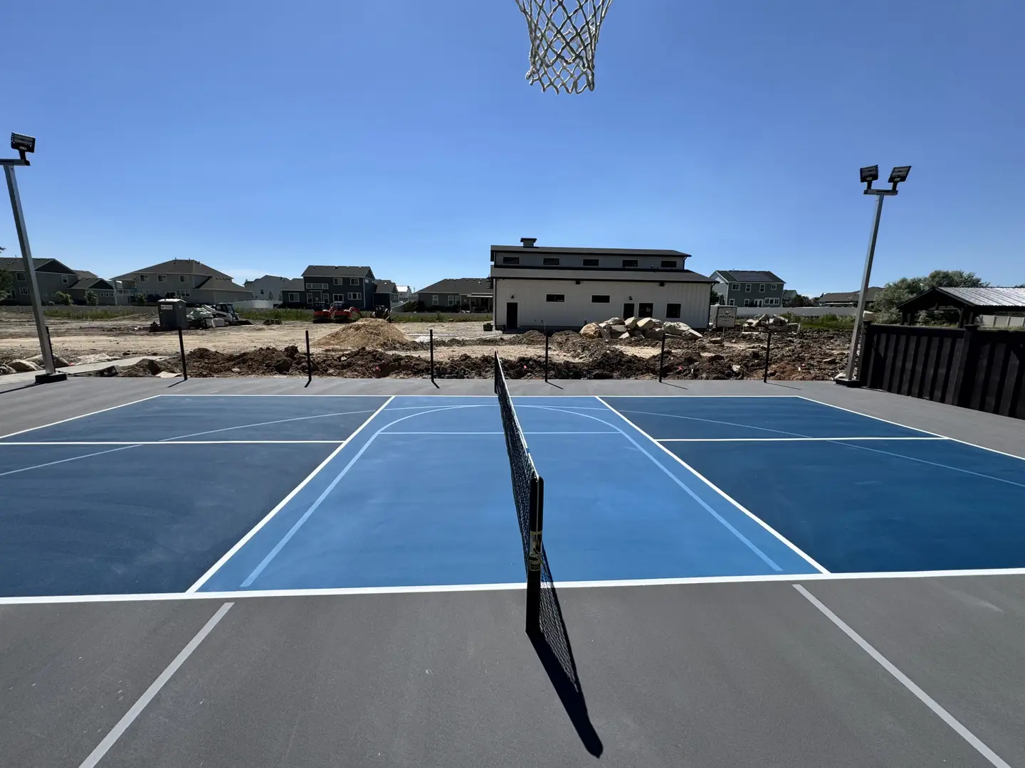 New blue pickleball court with basketball hoop and lights.