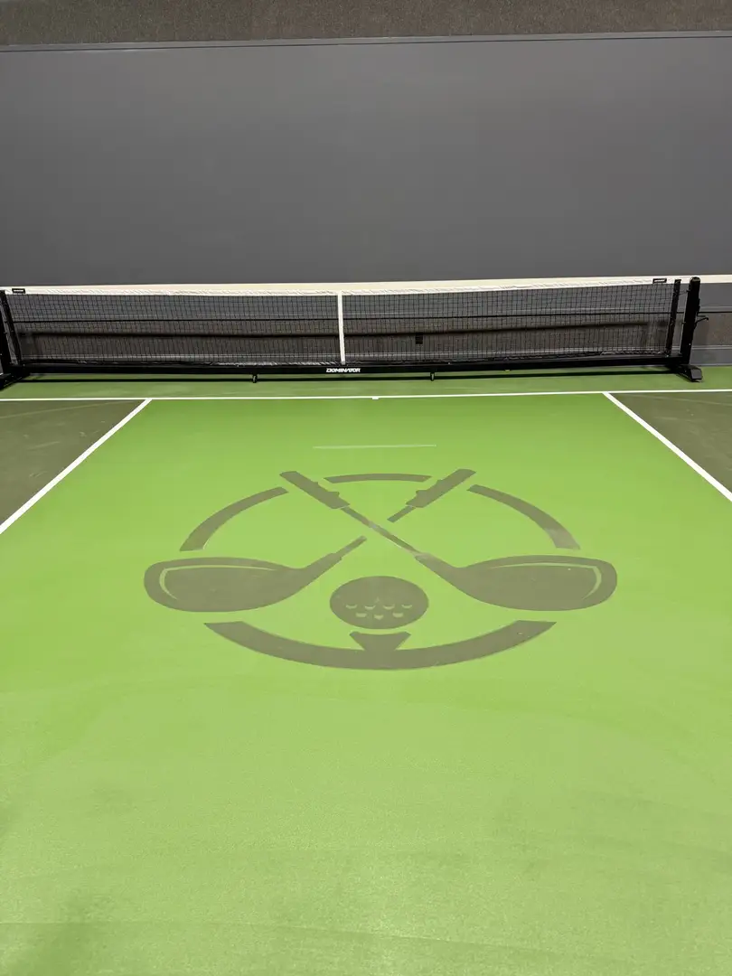 Indoor golf simulator court with crossed clubs and golf ball logo.