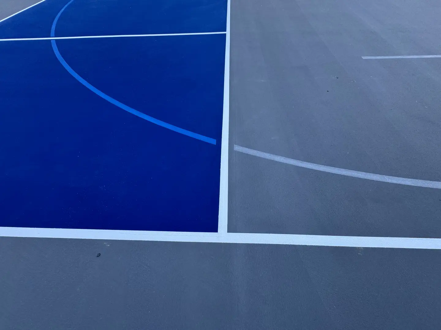Freshly painted blue and gray basketball court with white lines.