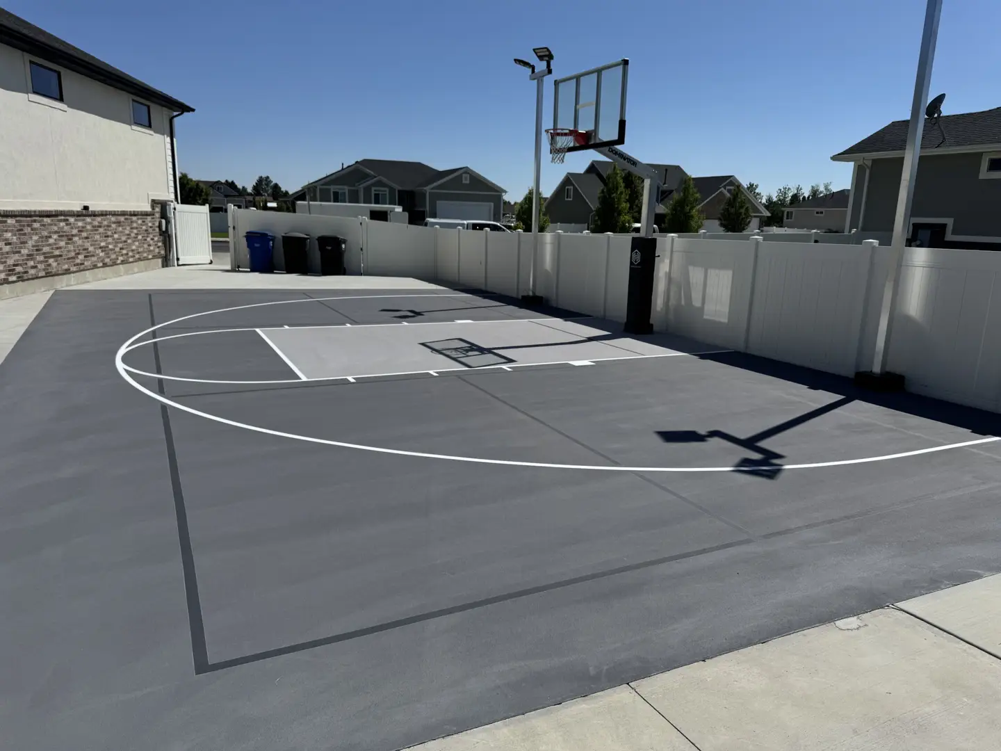 Modern backyard basketball court with grey surface and white lines.