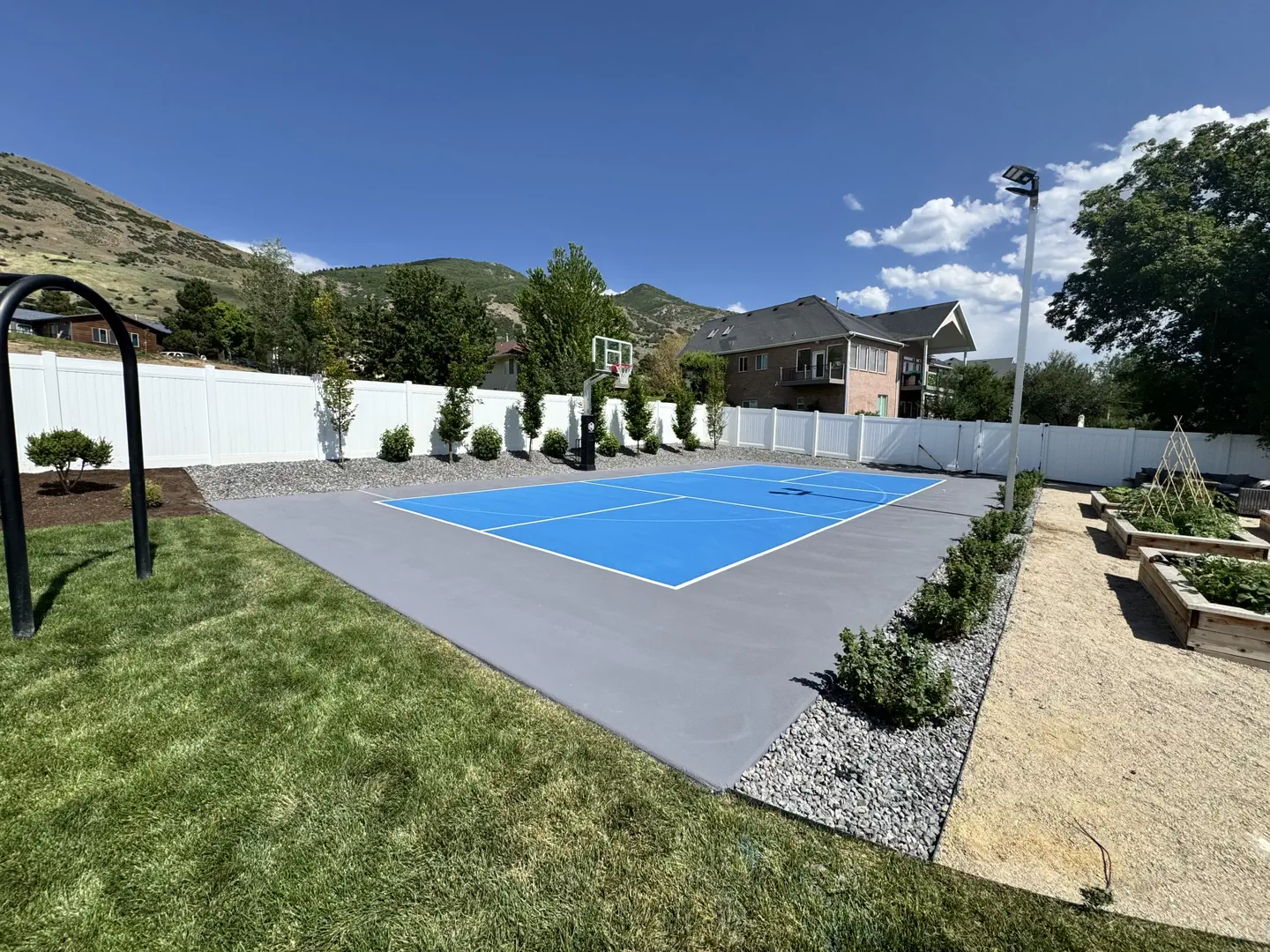 Blue and gray backyard sports court with basketball hoop and mountain backdrop.