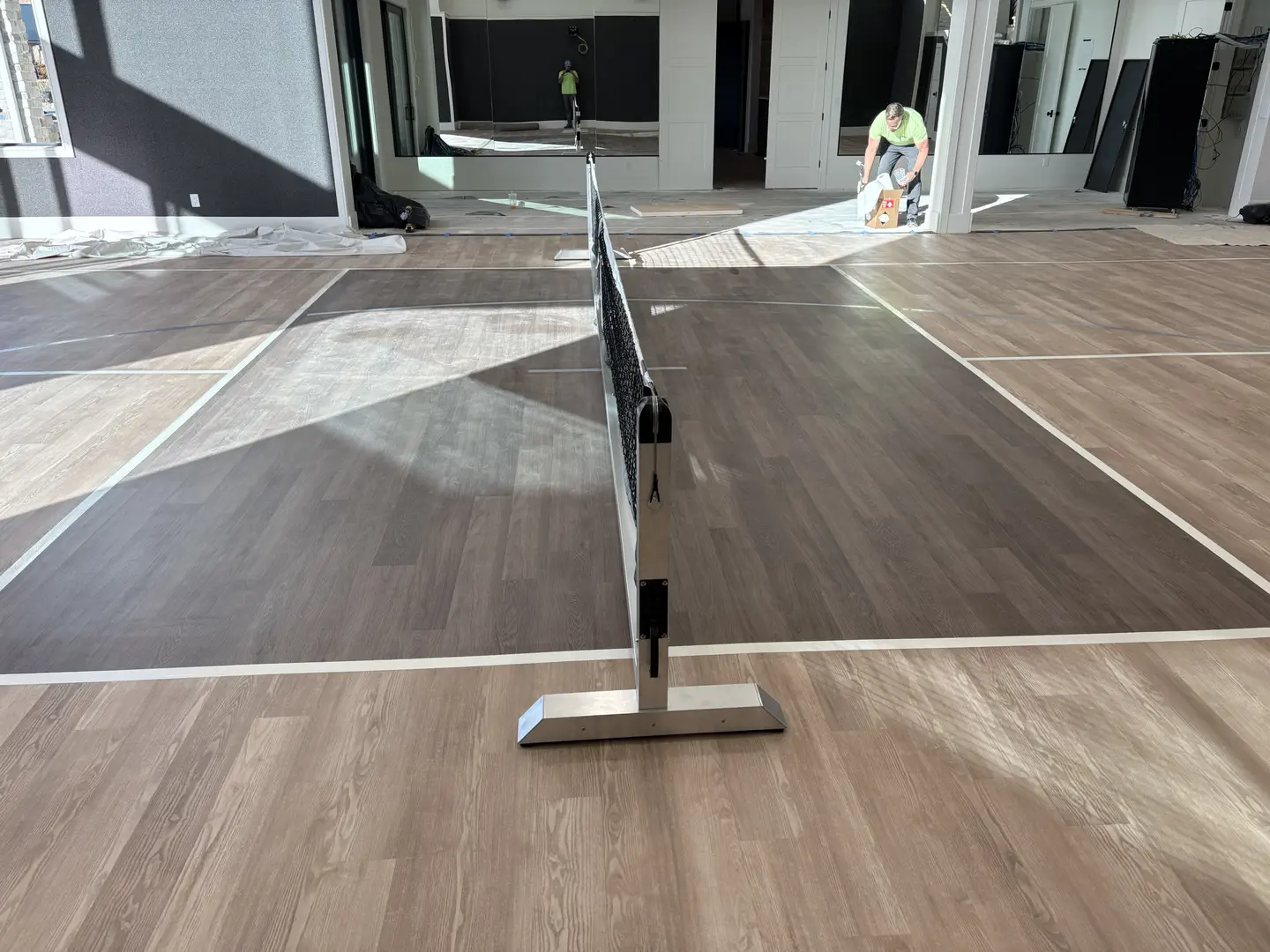 Indoor pickleball court with wood-look flooring and net.