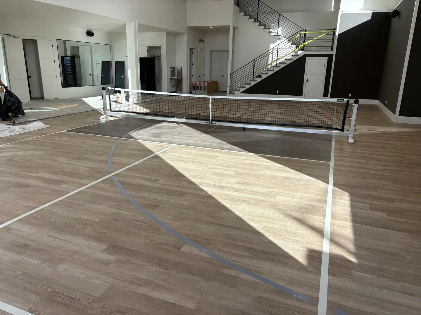 Indoor pickleball court with portable net and wood-look flooring.