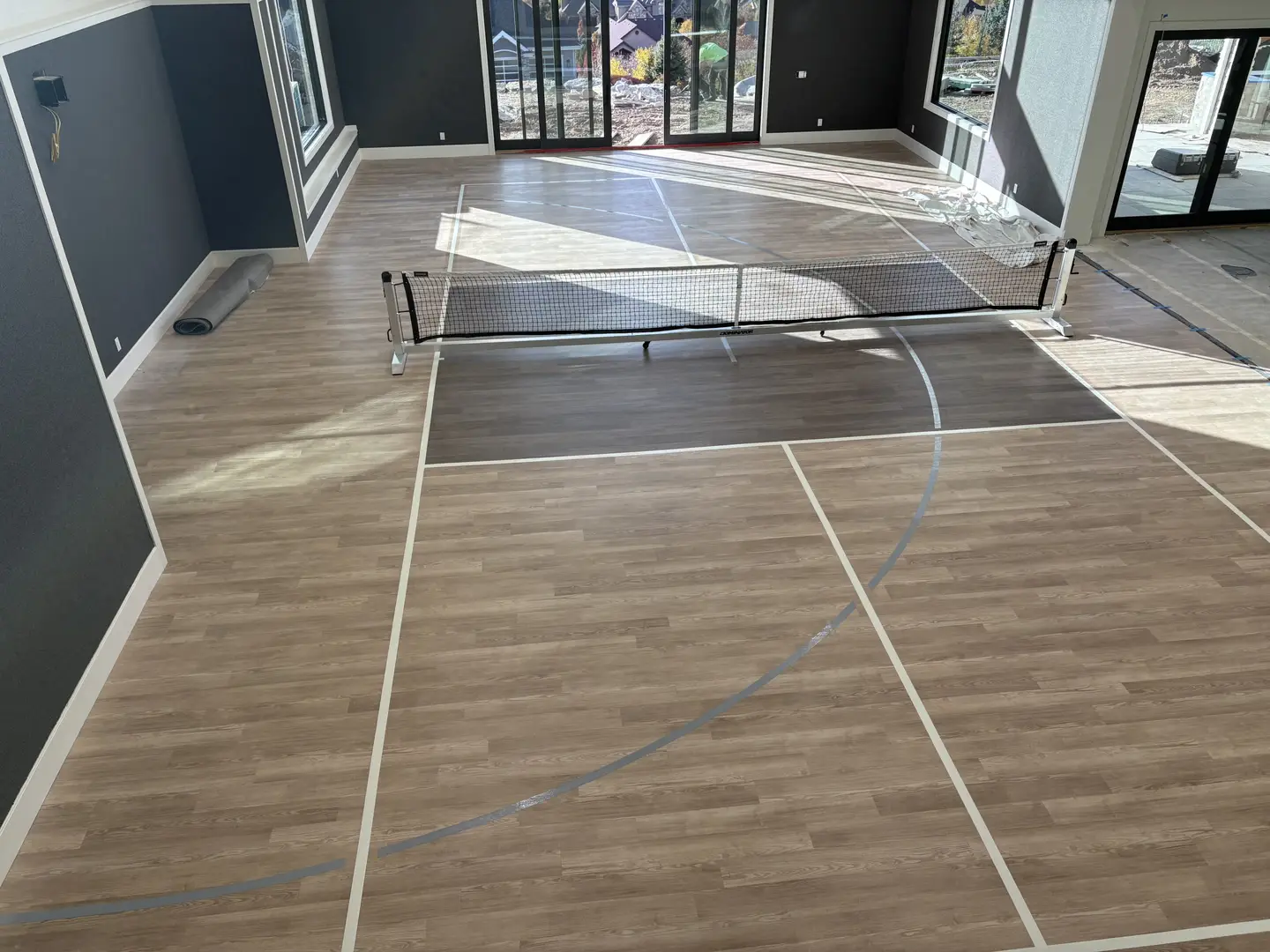 Indoor pickleball court with wood-look flooring and net.