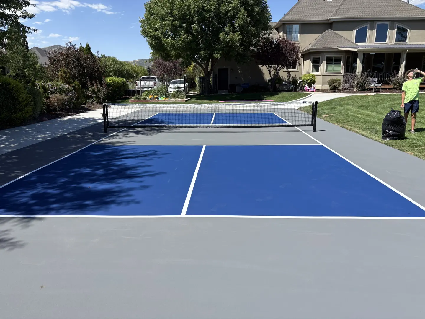 Newly painted blue and grey pickleball court in a residential backyard.