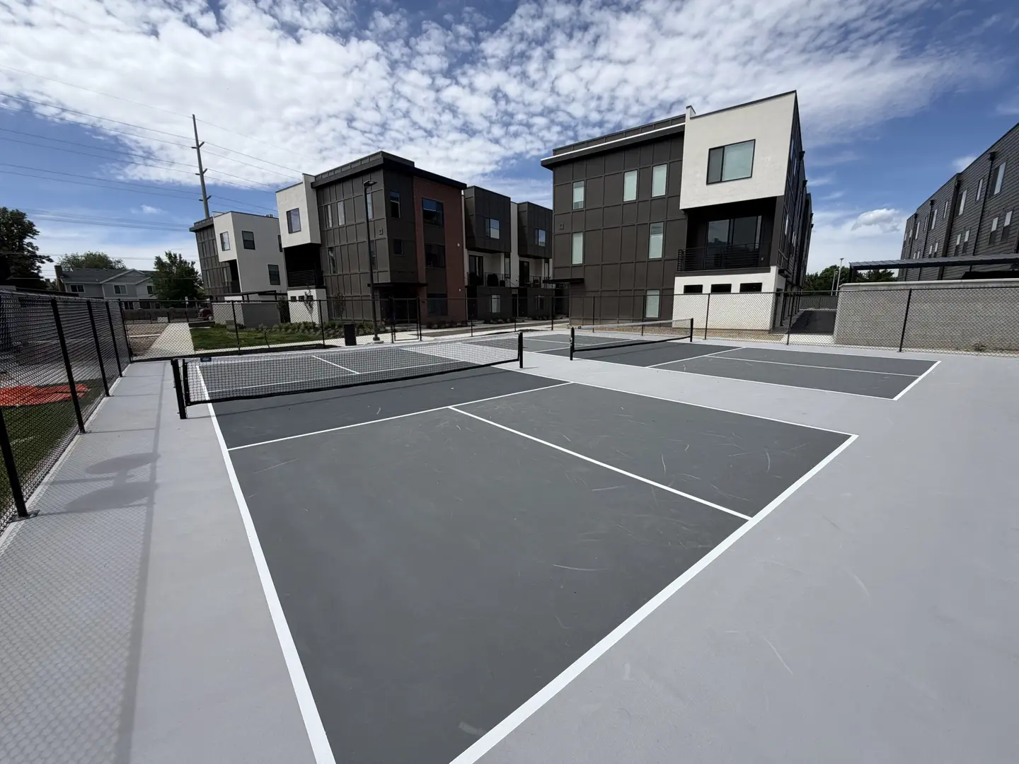 Modern townhomes overlook a clean pickleball court with multiple courts.