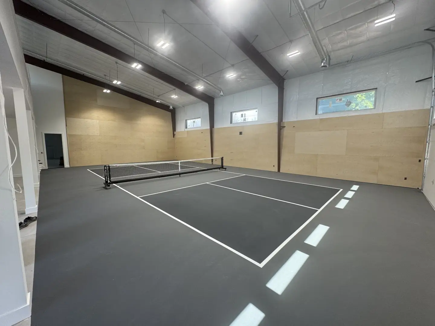 Indoor pickleball court with dark grey surface and white lines.