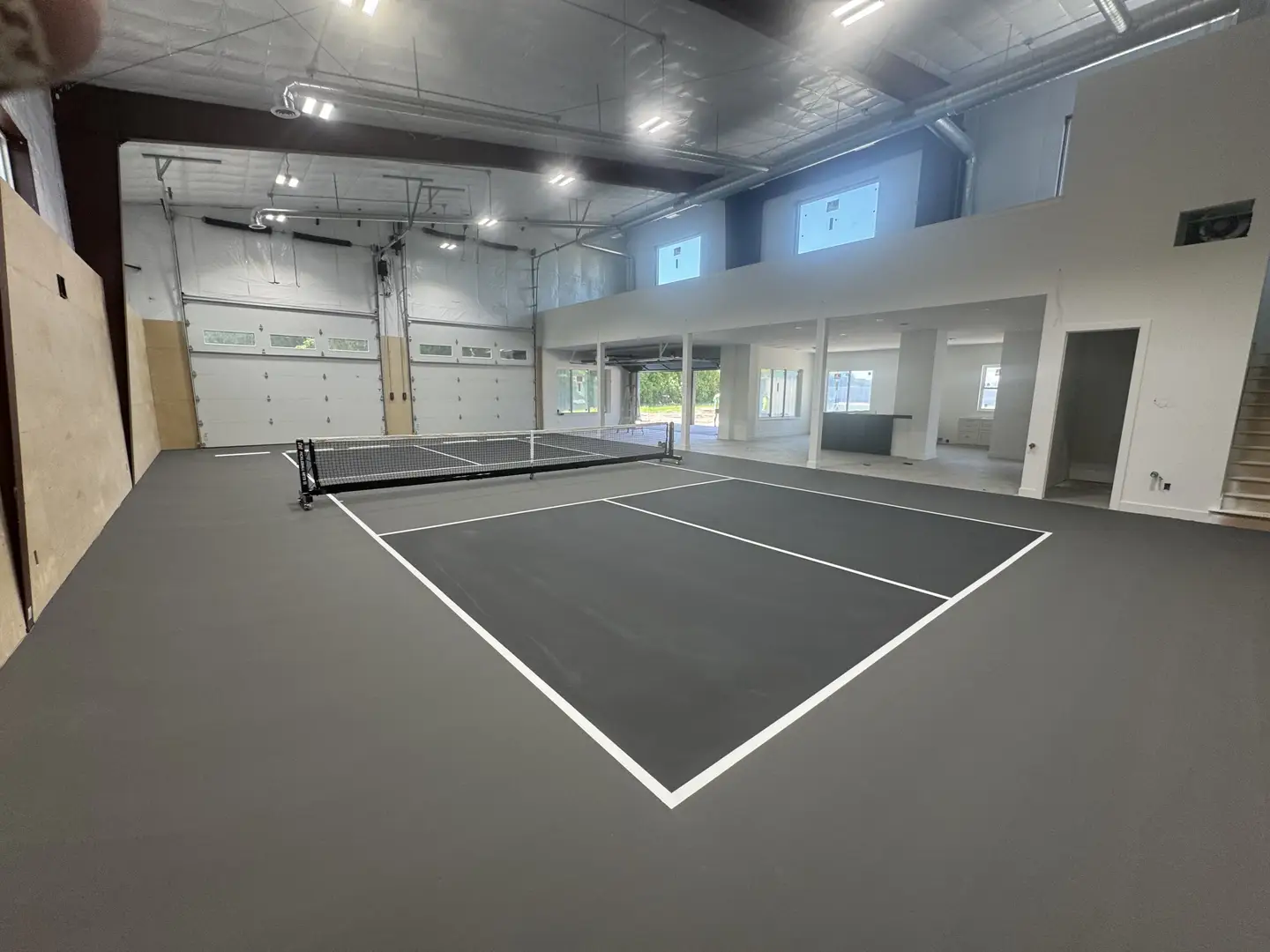 Indoor pickleball court with a modern loft and garage doors.