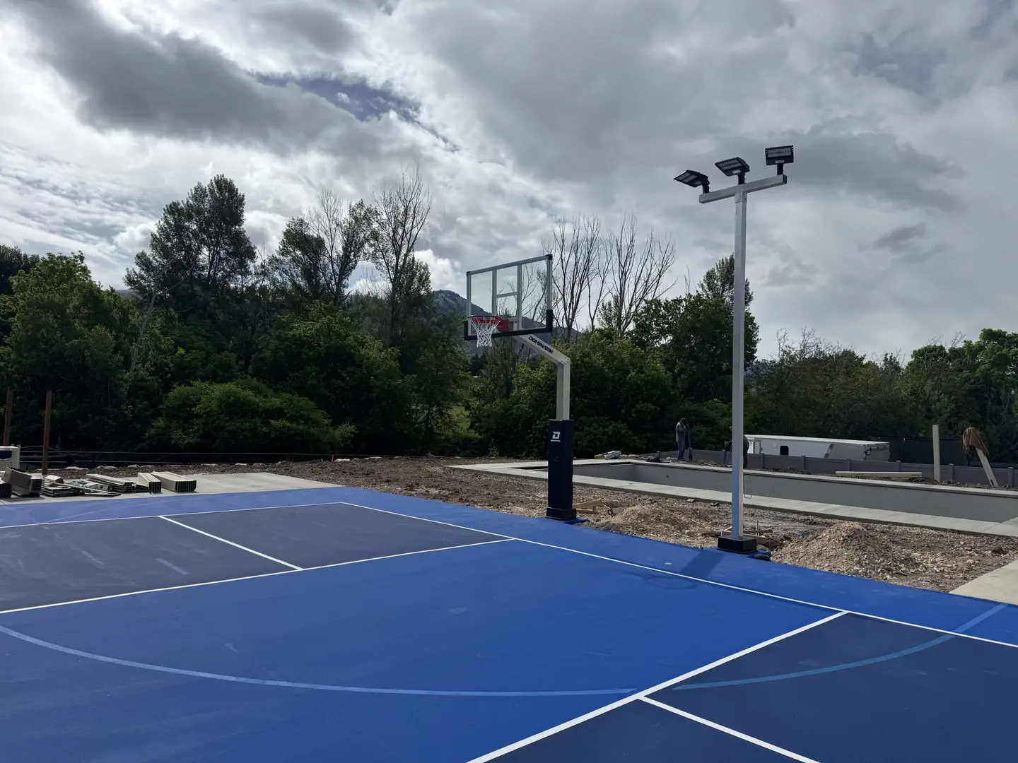 New blue basketball court with lights and trees in the background.