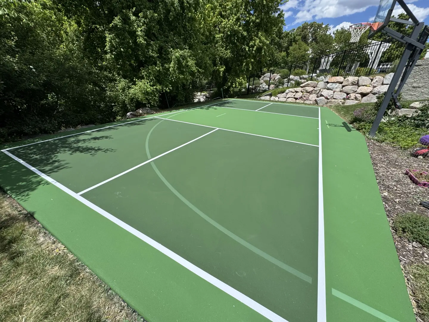 Newly painted green basketball and tennis court with white lines.