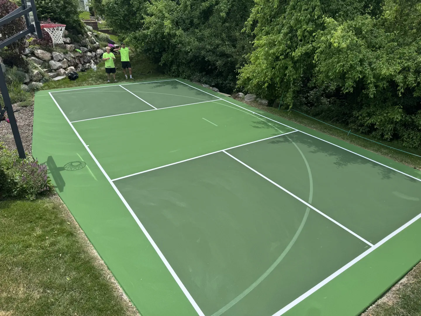 Newly painted green tennis court with white lines and two people on it.