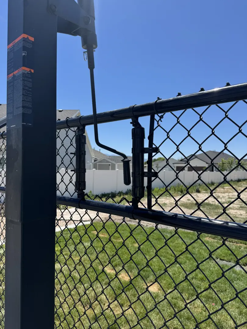 Black chain link fence gate latch mechanism with a blue sky background.