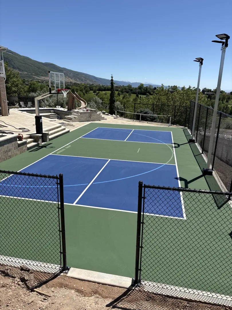 Multi-sport court with basketball hoop and pickleball lines, overlooking a scenic landscape.