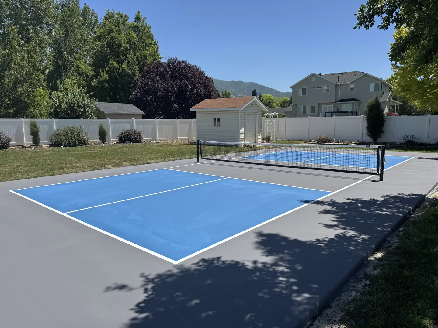 Newly painted blue pickleball court with white lines in a suburban backyard.