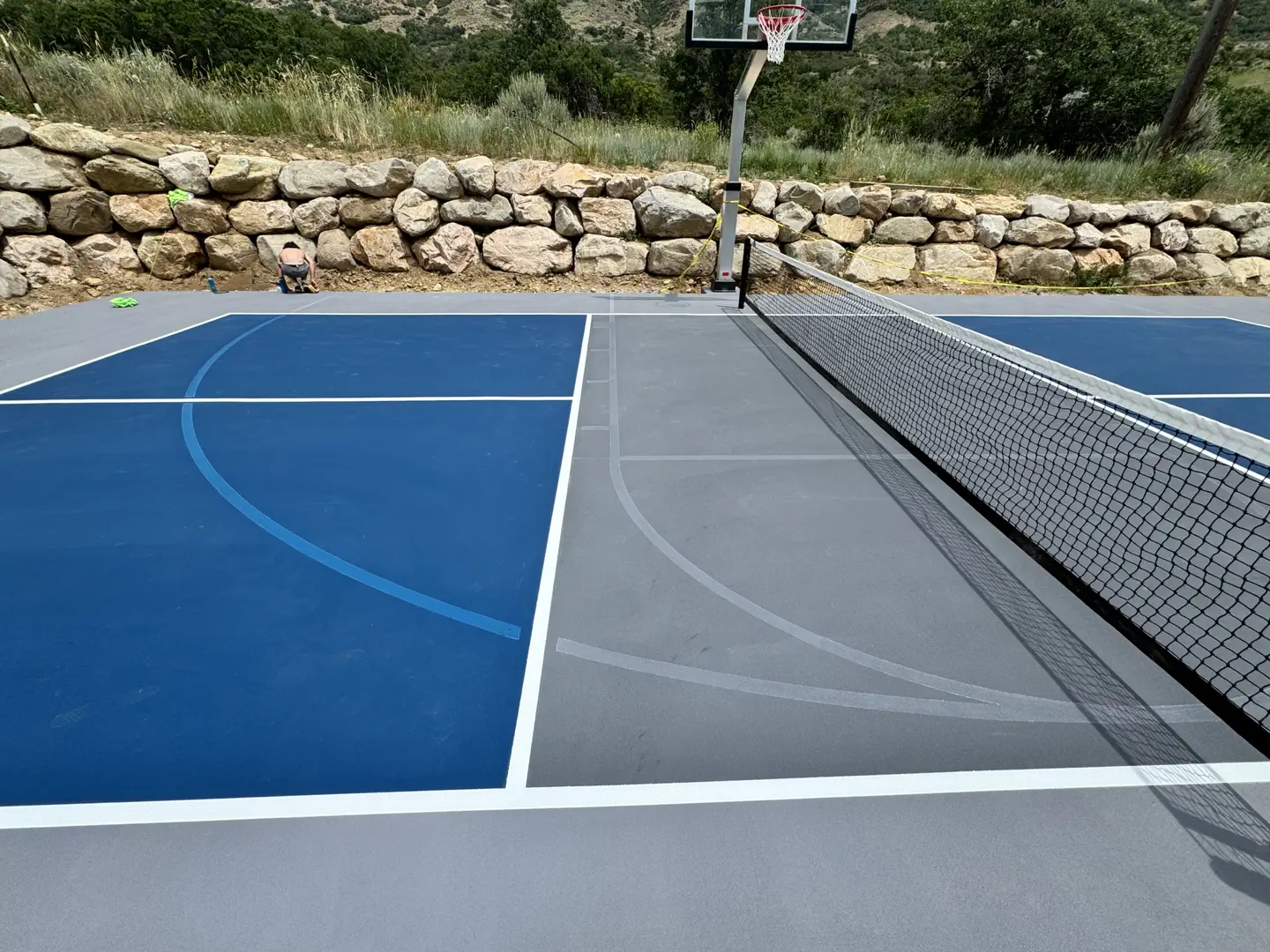 Newly painted blue and gray pickleball court with basketball hoop and net
