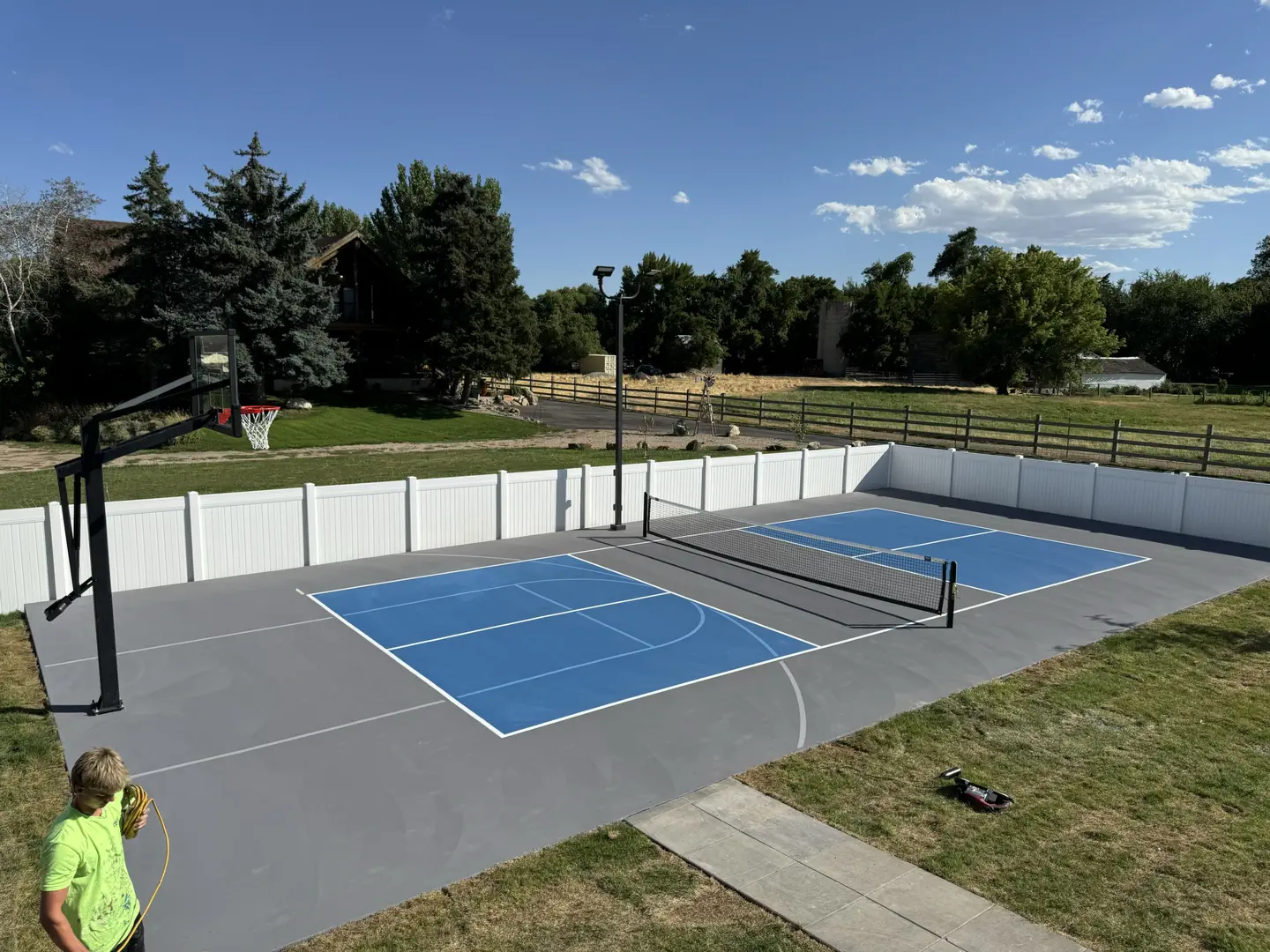 Backyard pickleball and basketball court with blue playing surfaces.