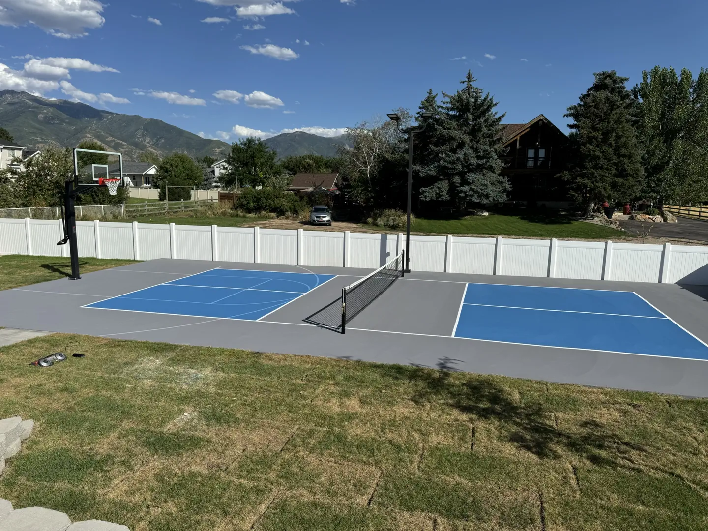 Multi-sport court with basketball hoop and pickleball net in a backyard.
