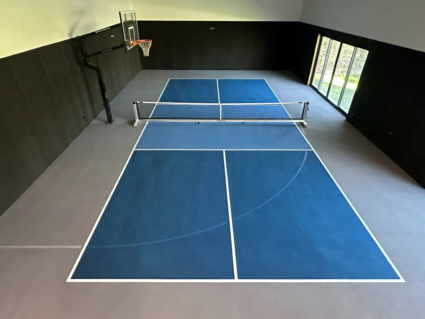 Indoor pickleball court with basketball hoop and large windows