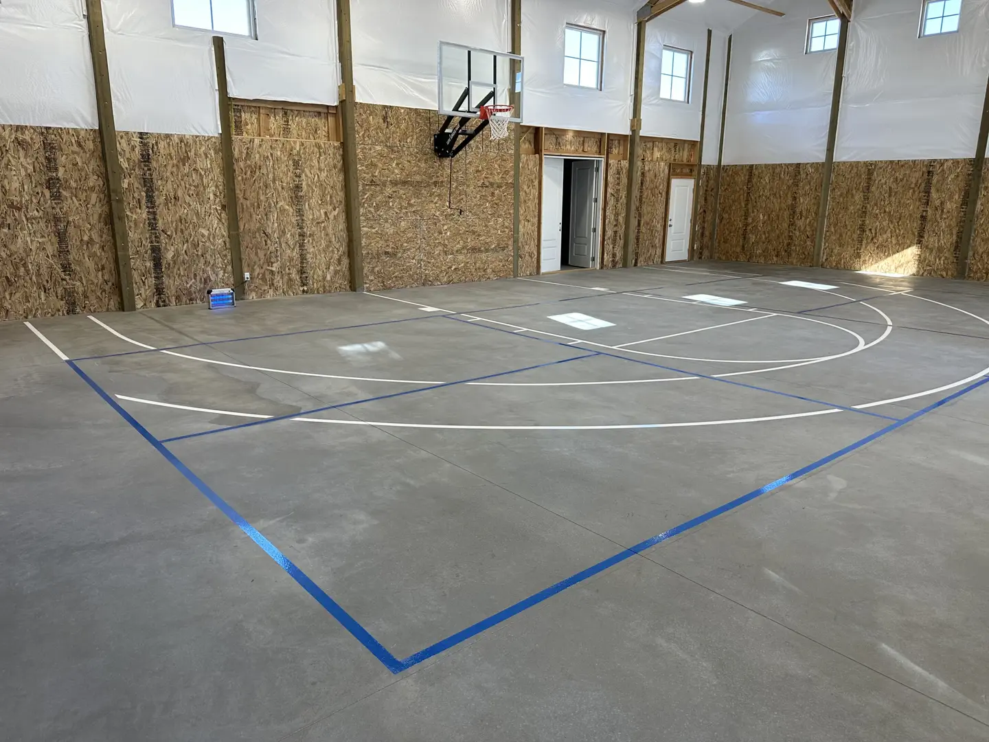 Indoor basketball court with concrete floor and blue and white lines.