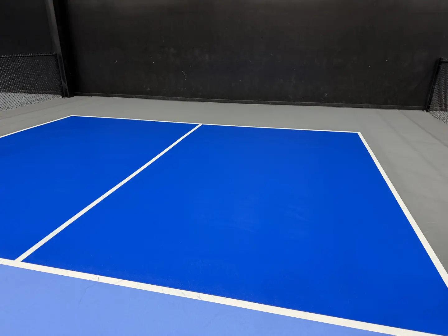 Bright blue indoor pickleball court with white lines.