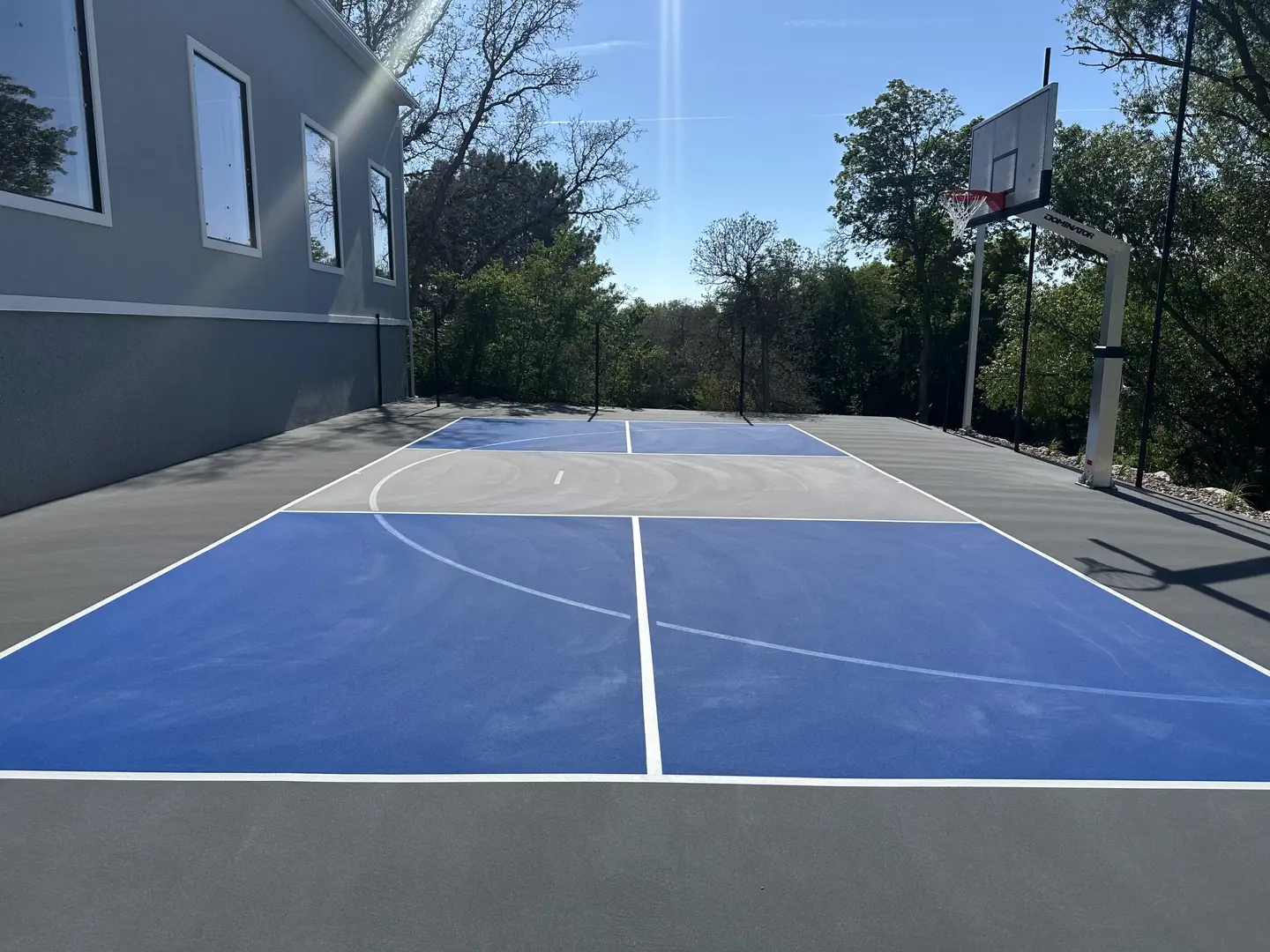 Blue and gray basketball court with hoop and trees in background