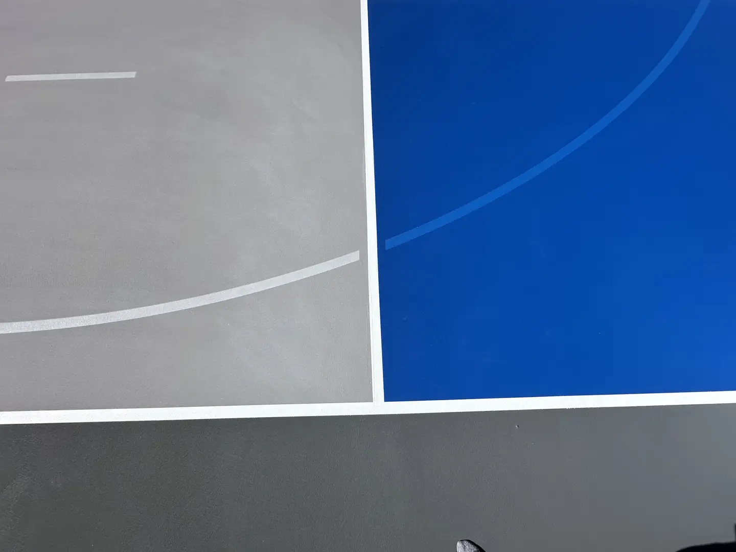 Newly painted basketball court with blue and gray sections and white lines.
