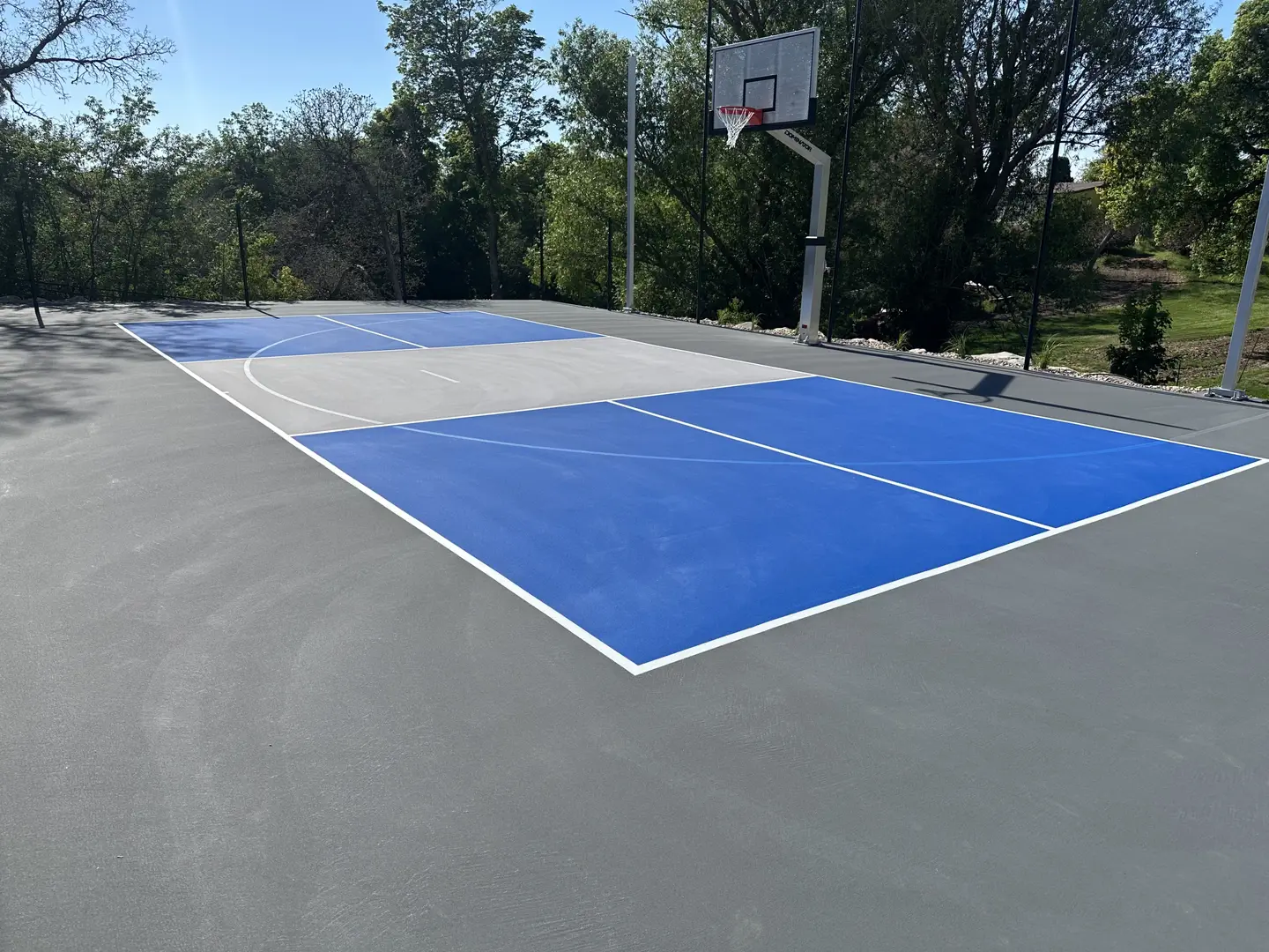New blue and grey basketball court with hoop and trees.
