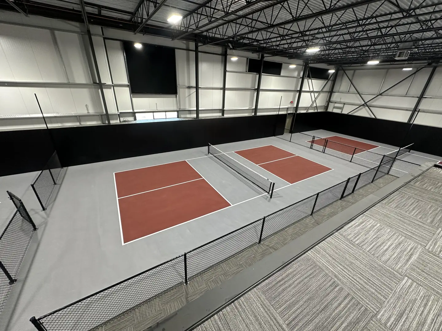 Indoor pickleball courts with red playing surfaces and gray surrounds.
