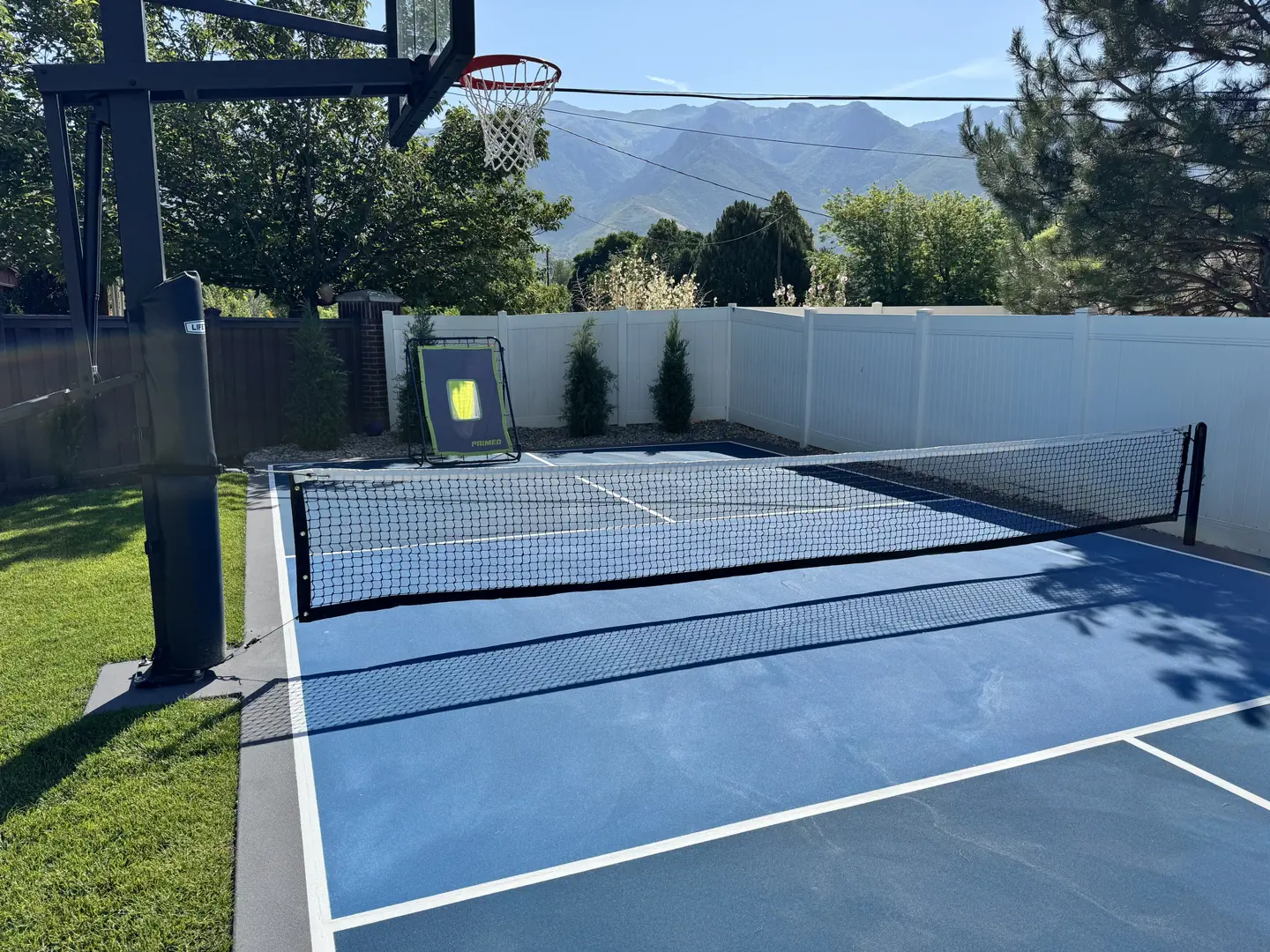 Blue pickleball court with basketball hoop and mountains in background