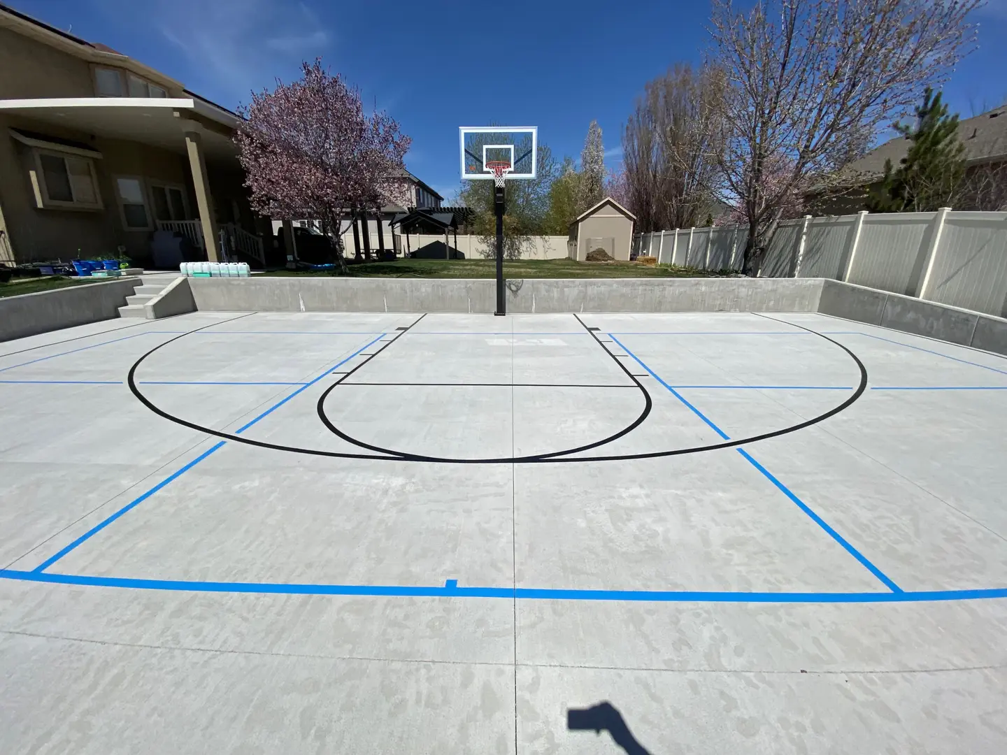 Newly constructed concrete basketball court with blue lines and a hoop.