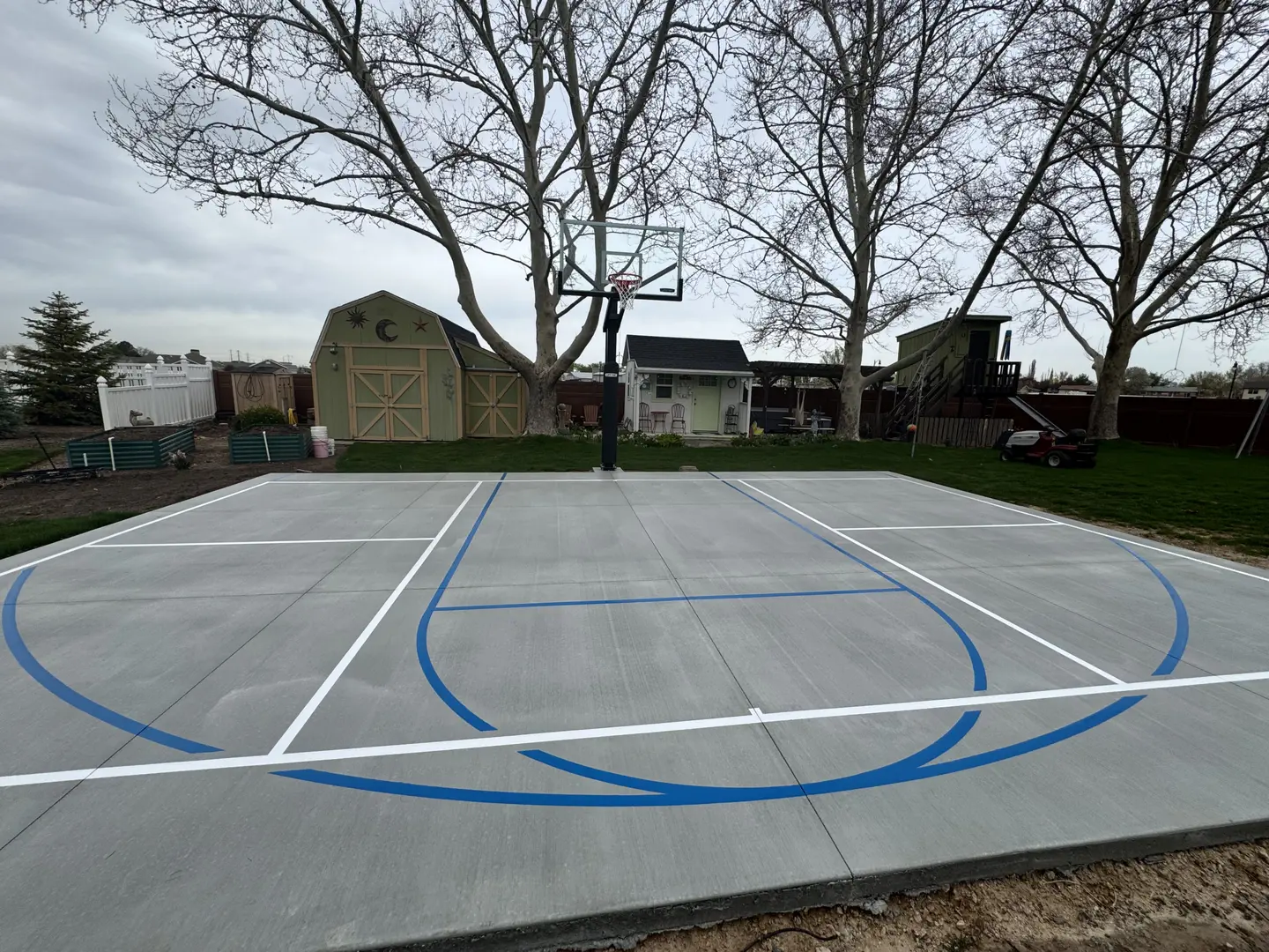 Newly painted basketball court in a backyard with a basketball hoop.