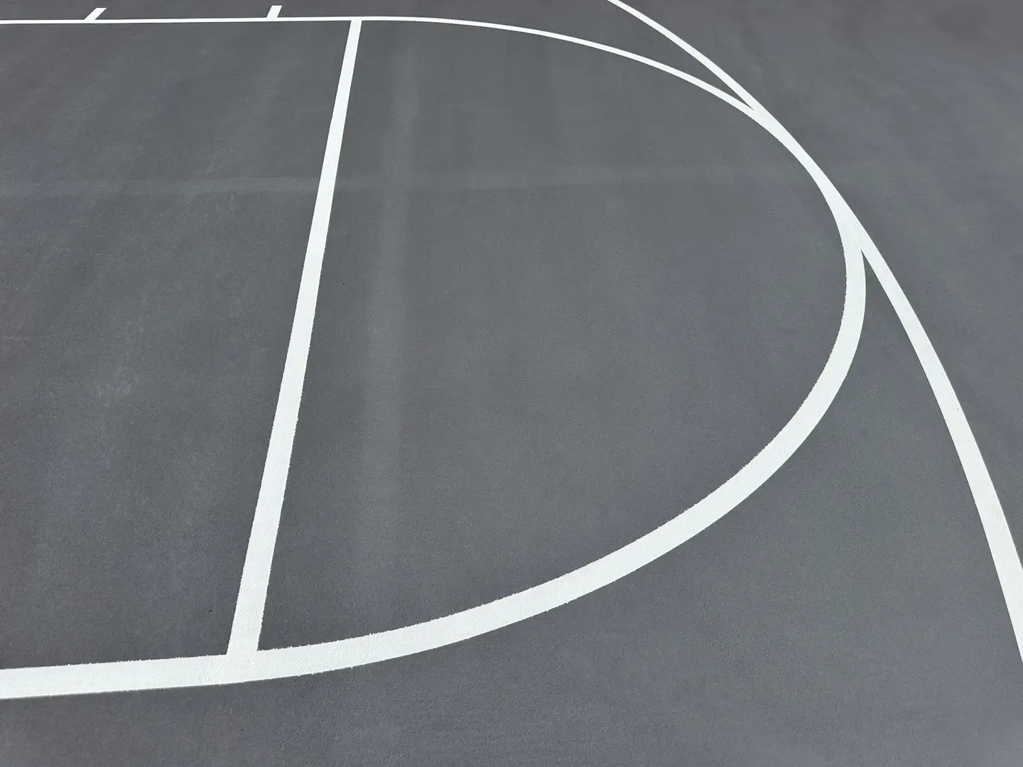 Close-up of a newly painted basketball court with white lines on a grey surface.
